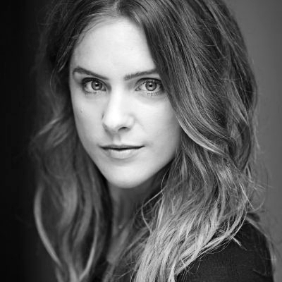 A black and white headshot of Kelly Gough. Kelly looks into the camera with a neutral expression.